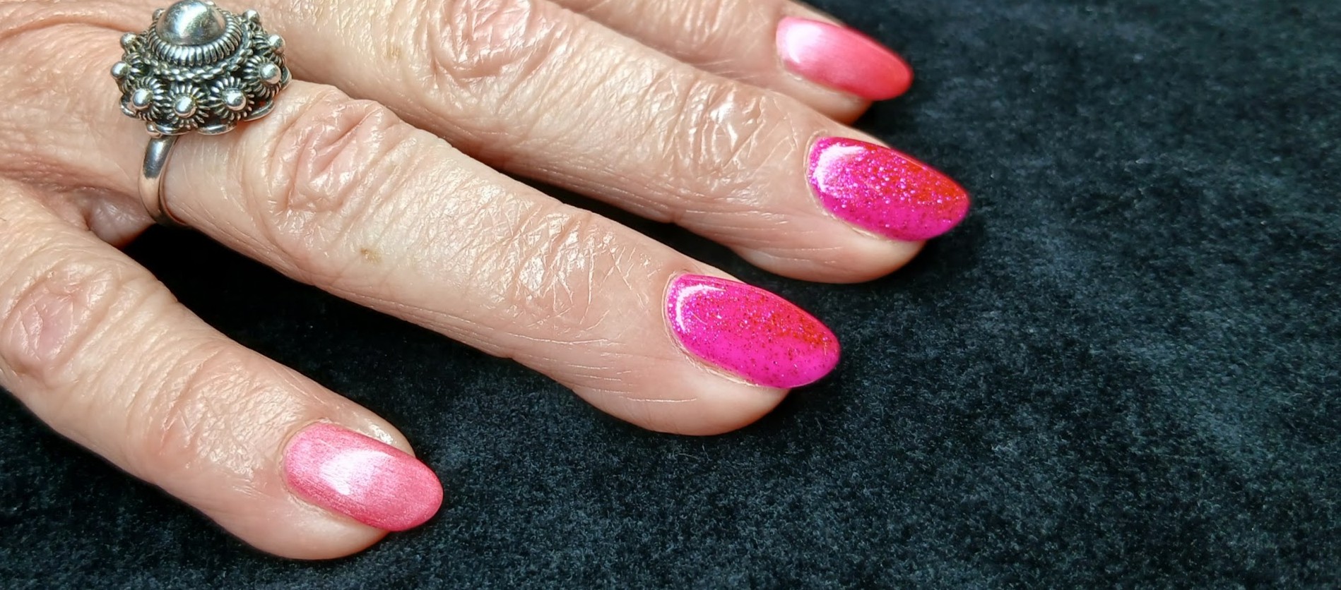 Roze ombré gellac met glitter, naast een zilveren ring