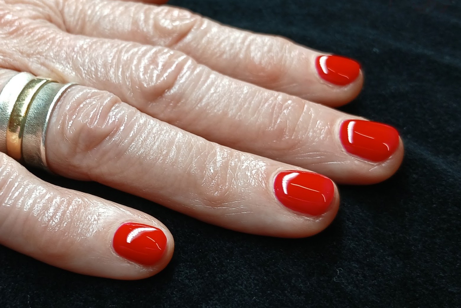 Glanzend rode gellac op natuurlijke nagels, op het donkere fluweel van de salon
